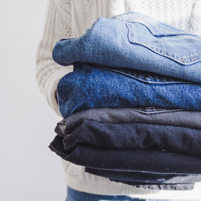 Photo. Image of a person holdings a stack of folded jeans of varying colors.